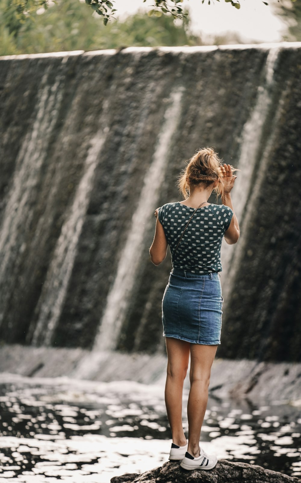 woman in blue and white polka dot dress standing in front of waterfalls during daytime