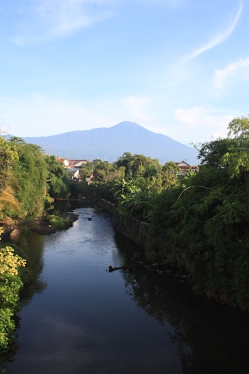 Luxury bungalow nestled in lush green mountains with a river flowing nearby under a bright blue sky.