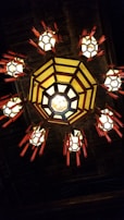 An ornate ceiling lamp with a central octagonal structure, emitting a warm glow. Surrounding the main light fixture are several smaller, similarly designed lights with red decorative tassels. The lighting pattern resembles a traditional style with intricate craftsmanship.