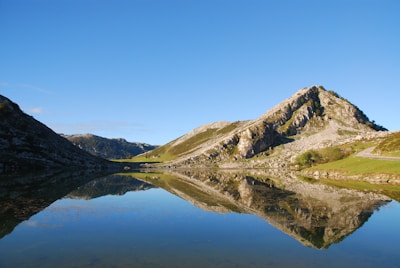 green and brown mountain beside lake under blue sky during daytime