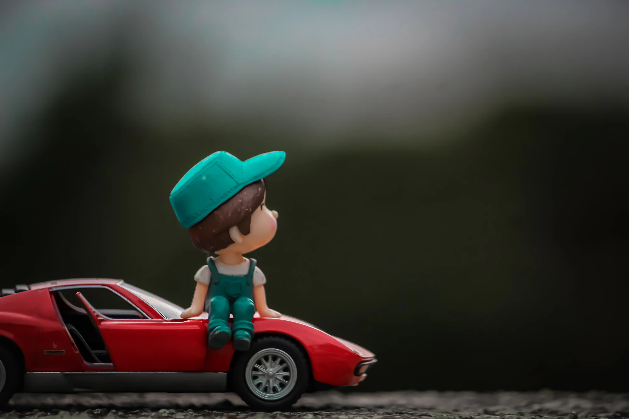 A small boy in a red cap sitting in a red ride-on toy car.