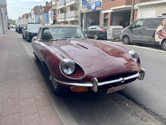 A gleaming red vintage convertible parked on a sunlit cobblestone street.