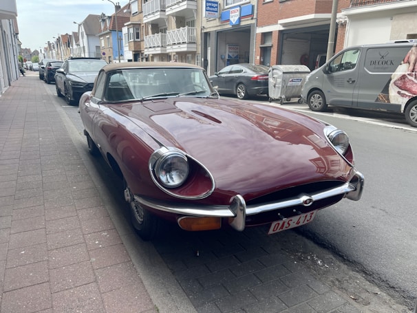 A gleaming red vintage convertible parked on a sunlit cobblestone street.