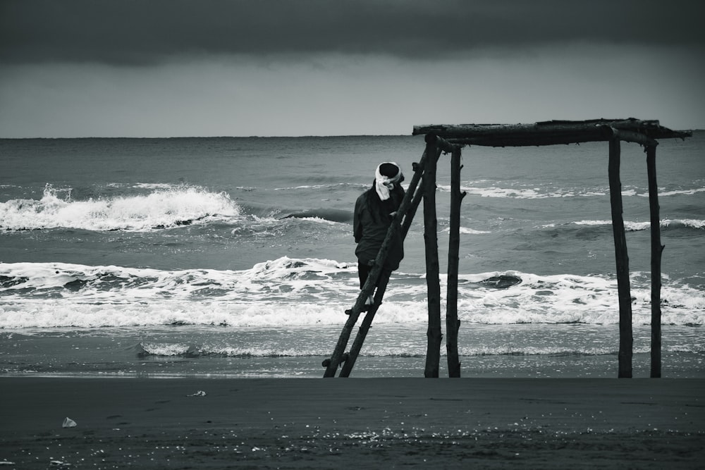 man in black jacket standing on wooden ladder on beach during daytime