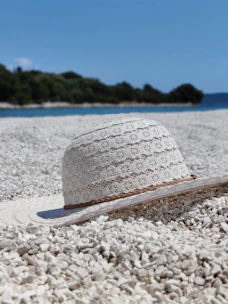 Elegant navy blue hat resting on white sand with soft ocean waves in background