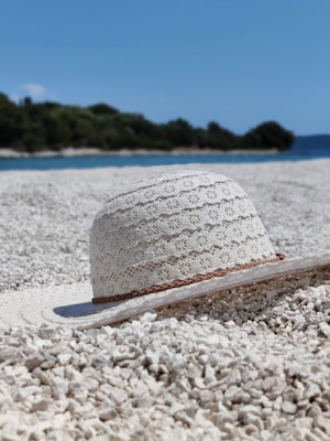 A sunlit beach scene featuring a straw summer hat with a red ribbon resting on a wooden table.