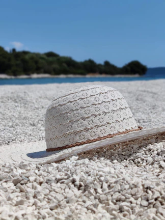 A close-up of a wide-brimmed straw sun hat resting on a beach towel with sunlight filtering through.