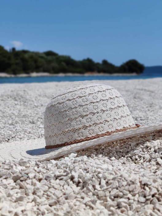 A sunlit beach scene featuring a straw summer hat with a red ribbon resting on a wooden table.