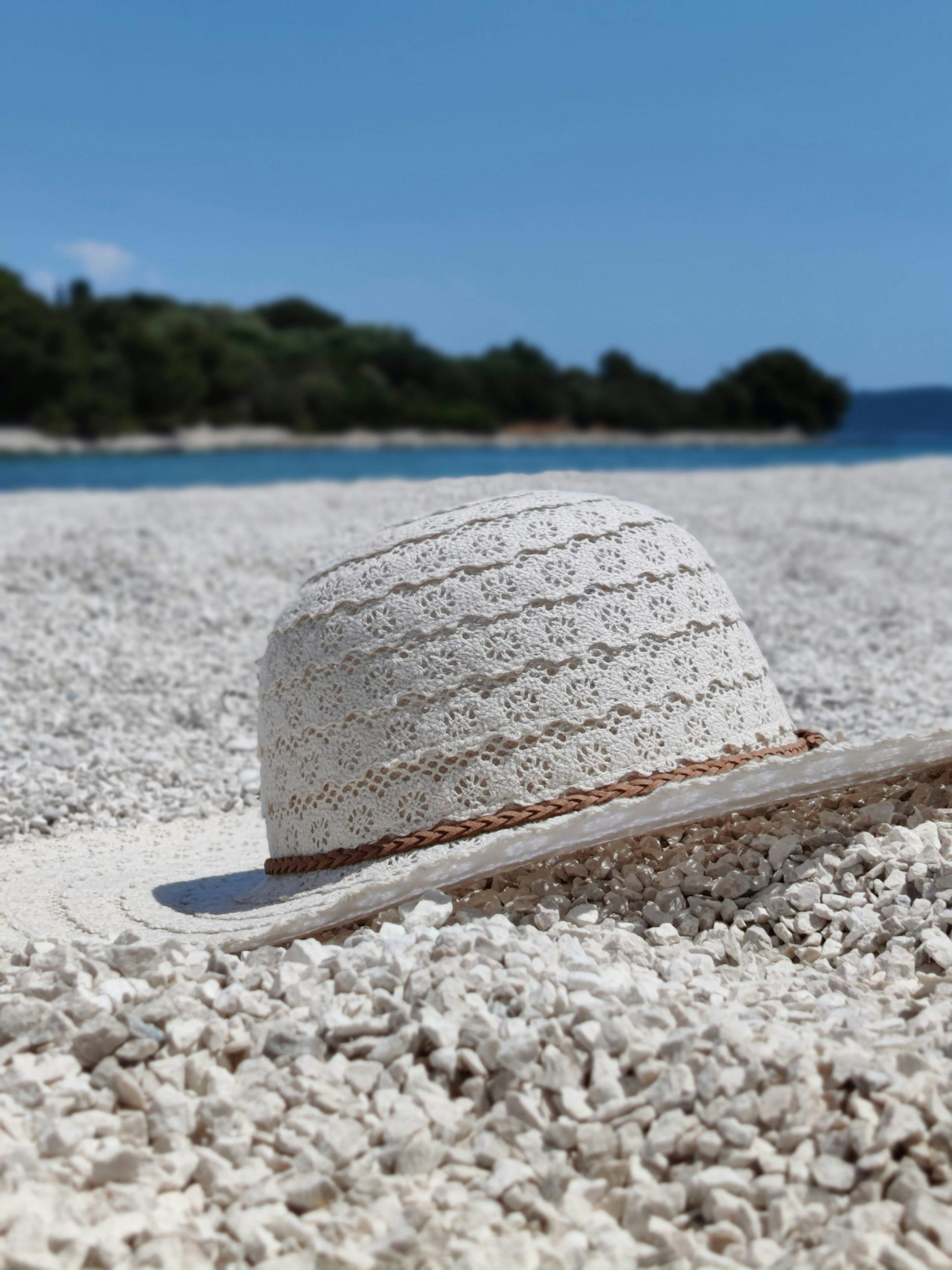 A sunlit close-up of a handcrafted straw beach hat with delicate woven details resting on soft white sand.