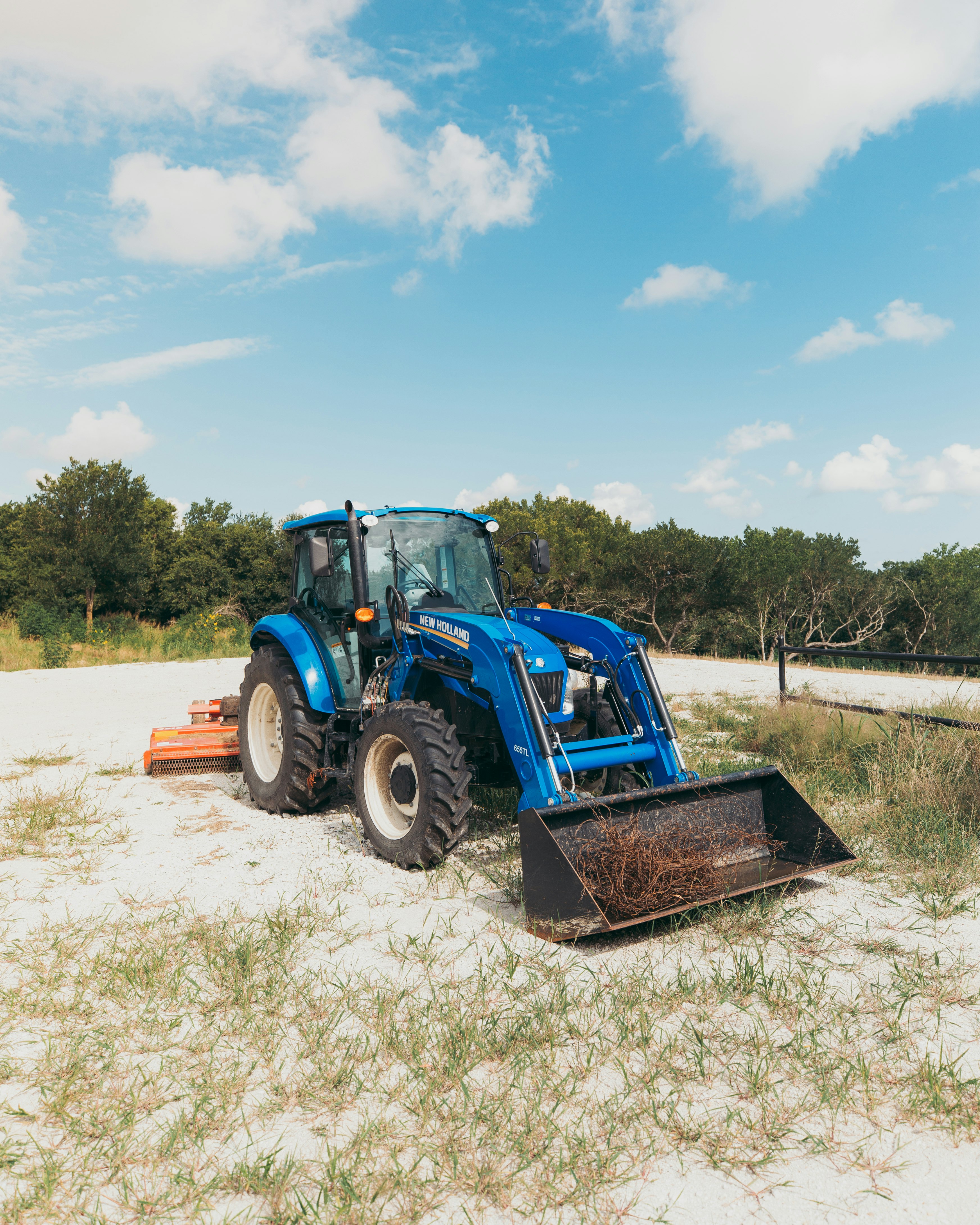 blue and black tractor on brown field under blue and white sunny cloudy sky during daytime