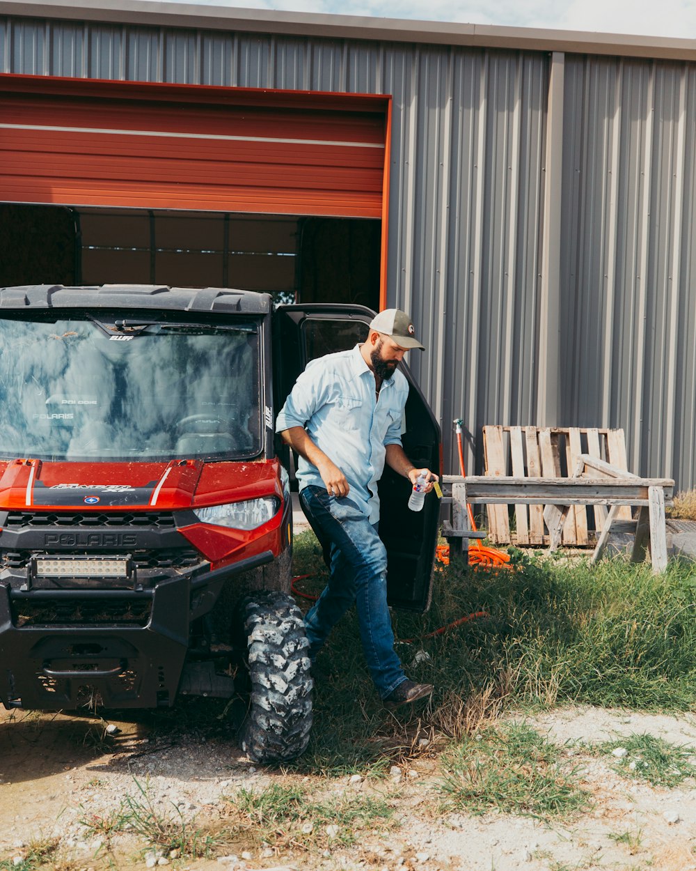 man in white long sleeve shirt and blue denim jeans standing beside red and black car