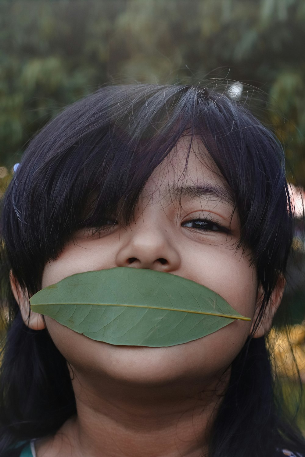 girl with black hair covering her face with green leaf