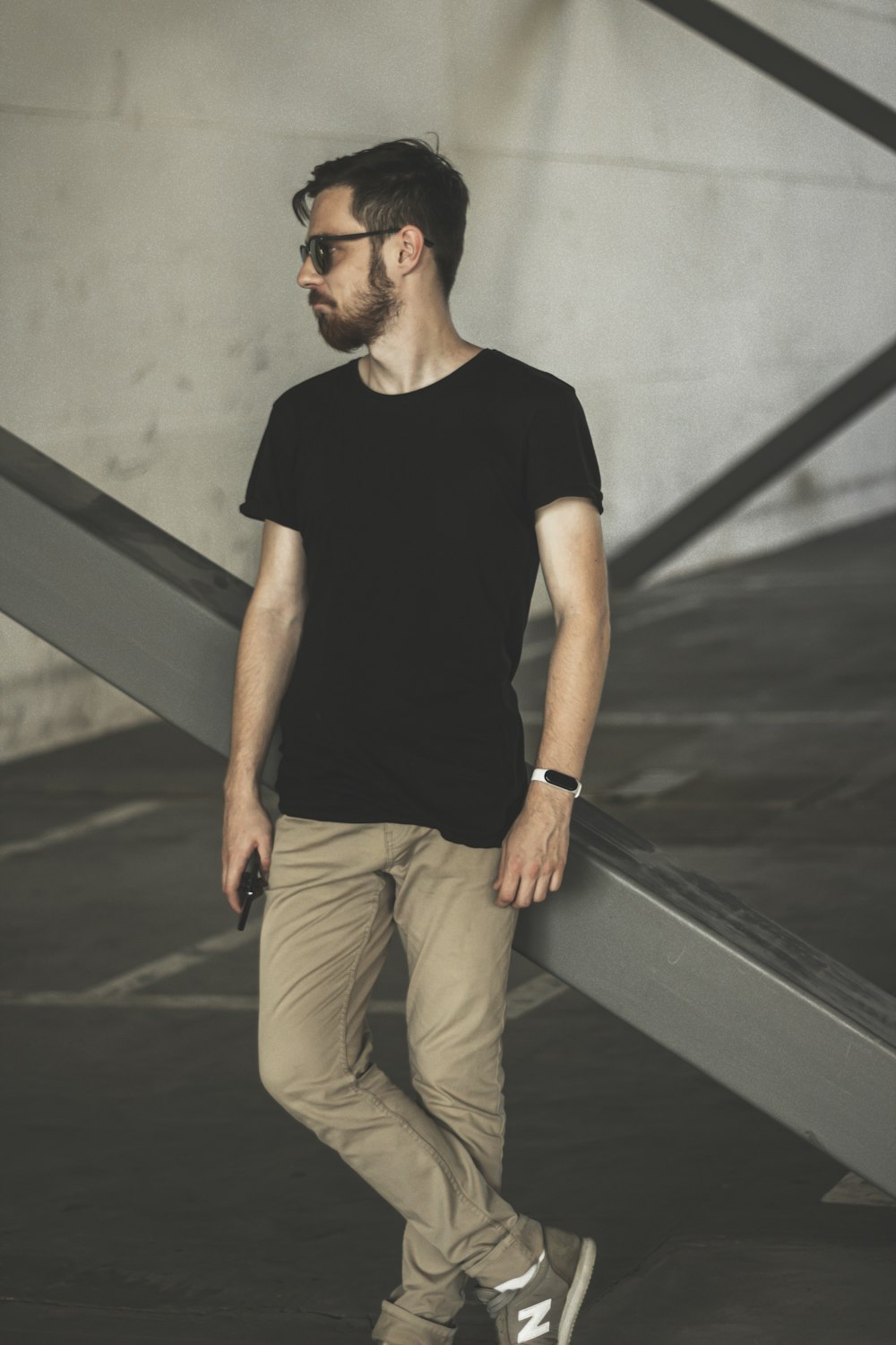 Uomo in t-shirt girocollo nera e pantaloni marroni seduto sul muro di cemento grigio