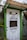 A doorway partially framed by green trim, featuring a sign that says 'PICK UP FOOD HERE' and another sign below with a QR code for scanning the menu. This is likely a service entrance for food pickup.