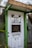 A doorway partially framed by green trim, featuring a sign that says 'PICK UP FOOD HERE' and another sign below with a QR code for scanning the menu. This is likely a service entrance for food pickup.