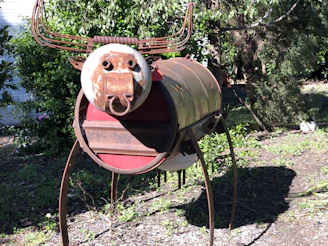 A whimsical sculpture assembled from discarded bicycle parts and scrap metal, standing in a garden.