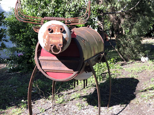 A whimsical sculpture assembled from discarded bicycle parts and scrap metal, standing in a garden.