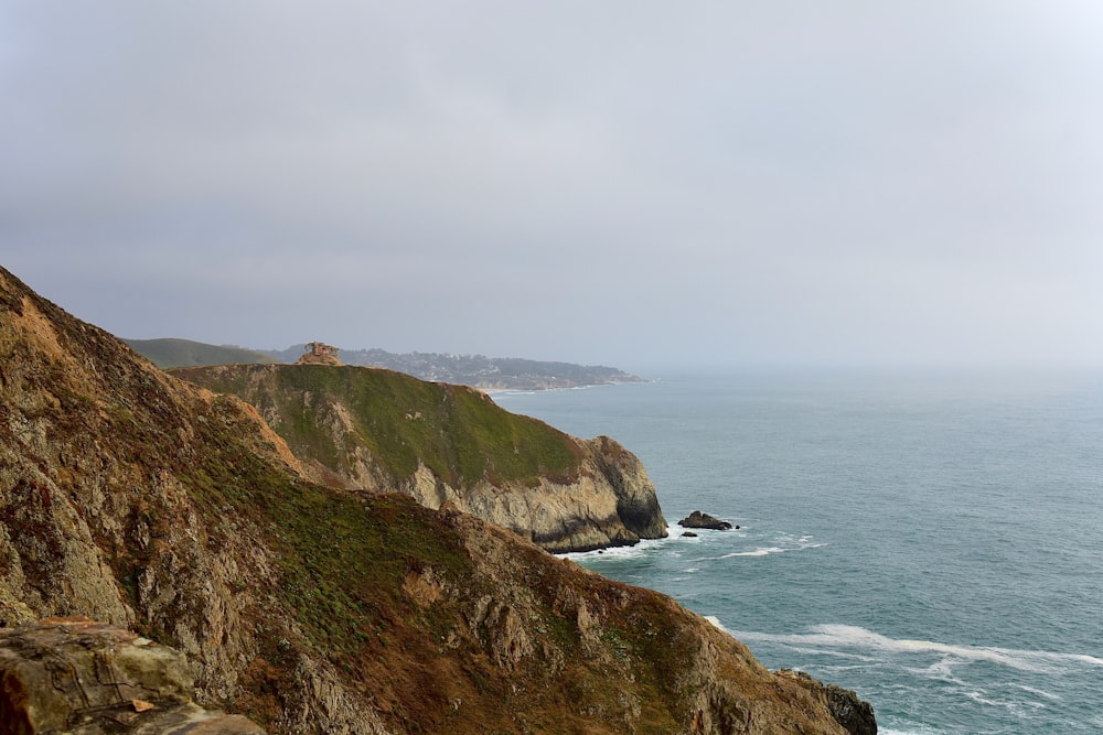 green and brown mountain beside sea under white sky during daytime