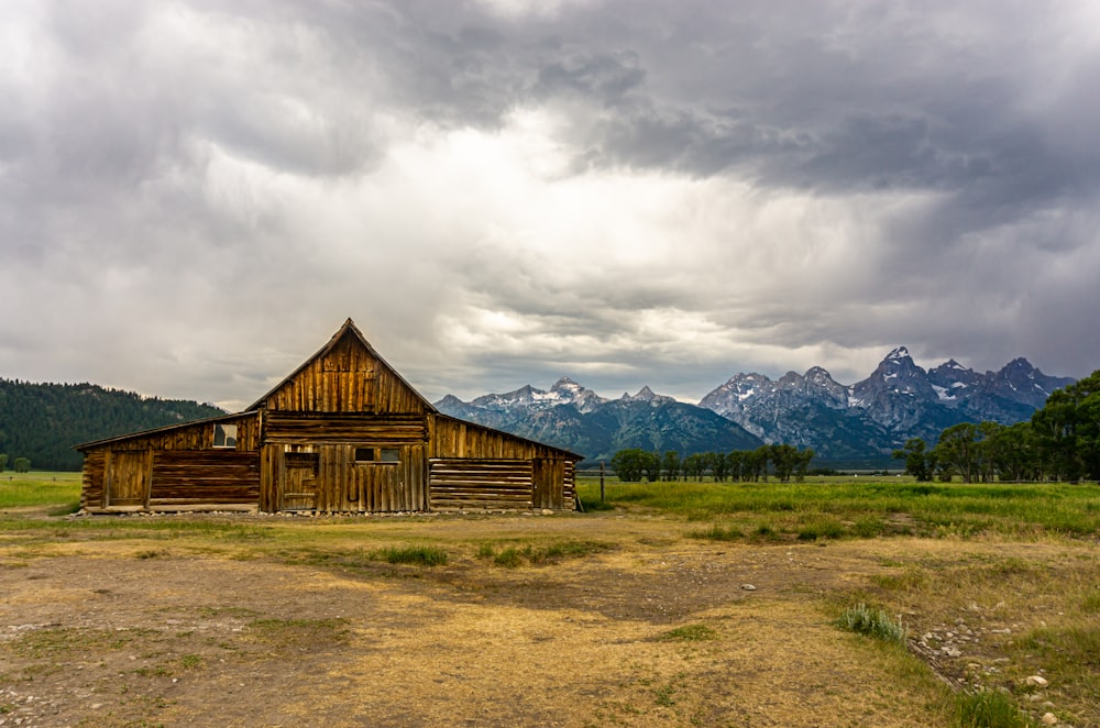 brown wooden house on green grass field near mountain under white clouds during daytime