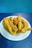 A plate filled with several pieces of deep-fried, battered catfish and a single hushpuppy. The fried catfish is golden brown and appears crispy, placed on a white plate with blue stripes. The setting has a blue textured background and tabletop.