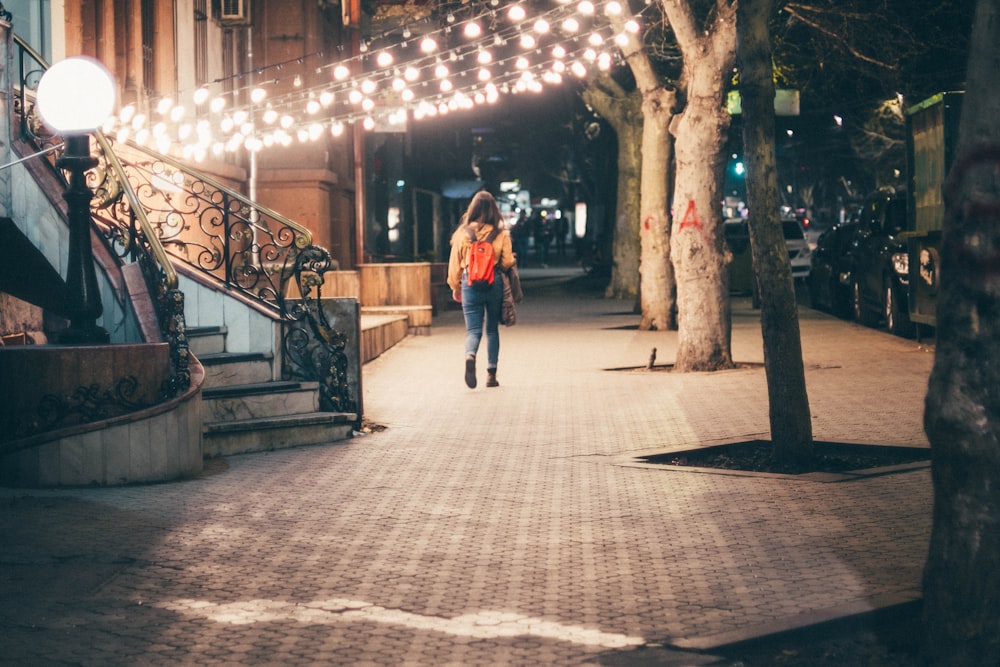 woman in red coat walking on sidewalk during night time