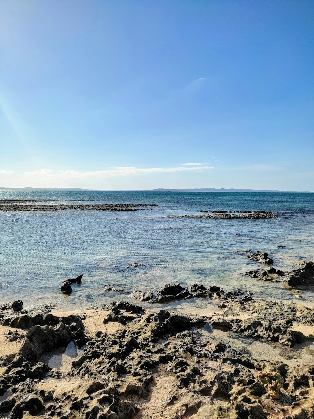 gray rocks on sea shore under blue sky during daytime