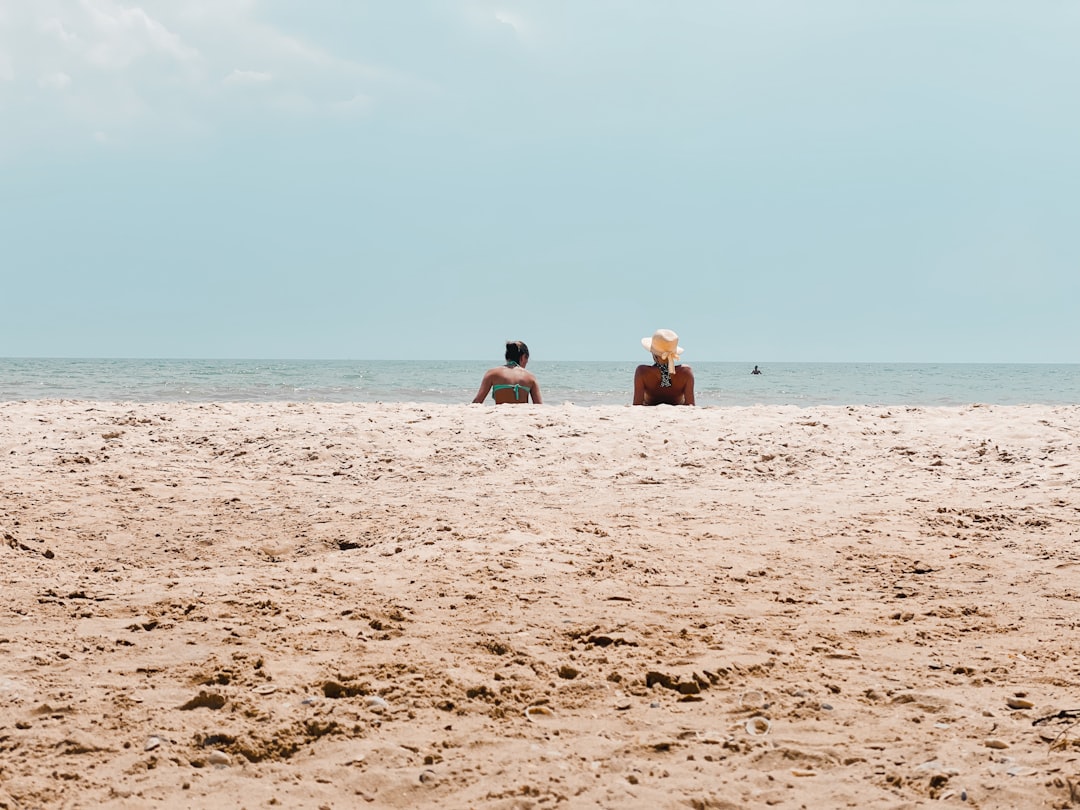 2 women sitting on beach sand during daytime