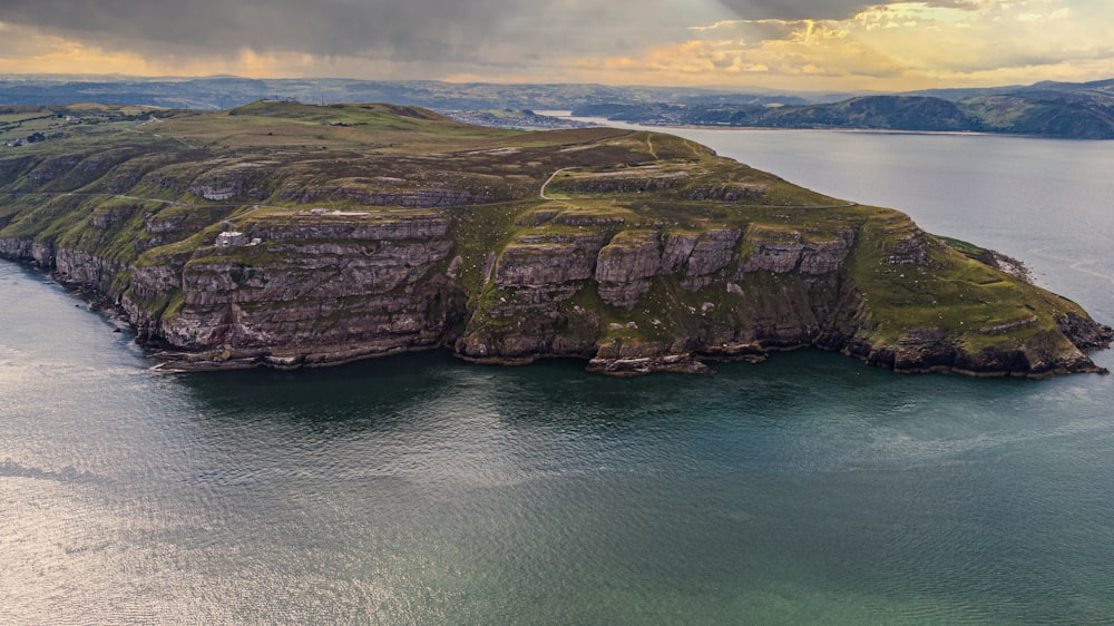 brown and green rock formation on blue sea under white clouds during daytime