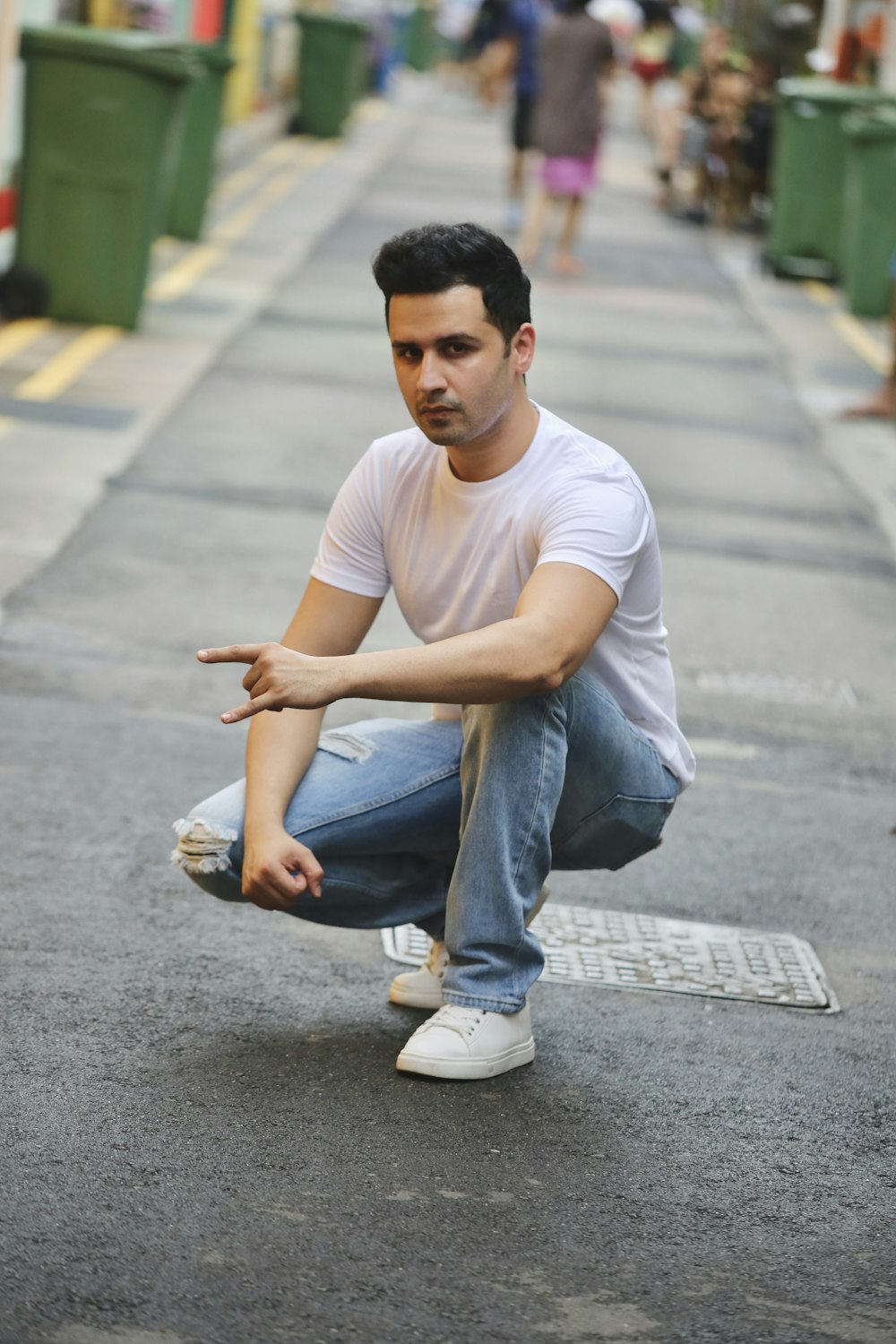 man in white crew neck t-shirt and blue denim jeans sitting on gray concrete road