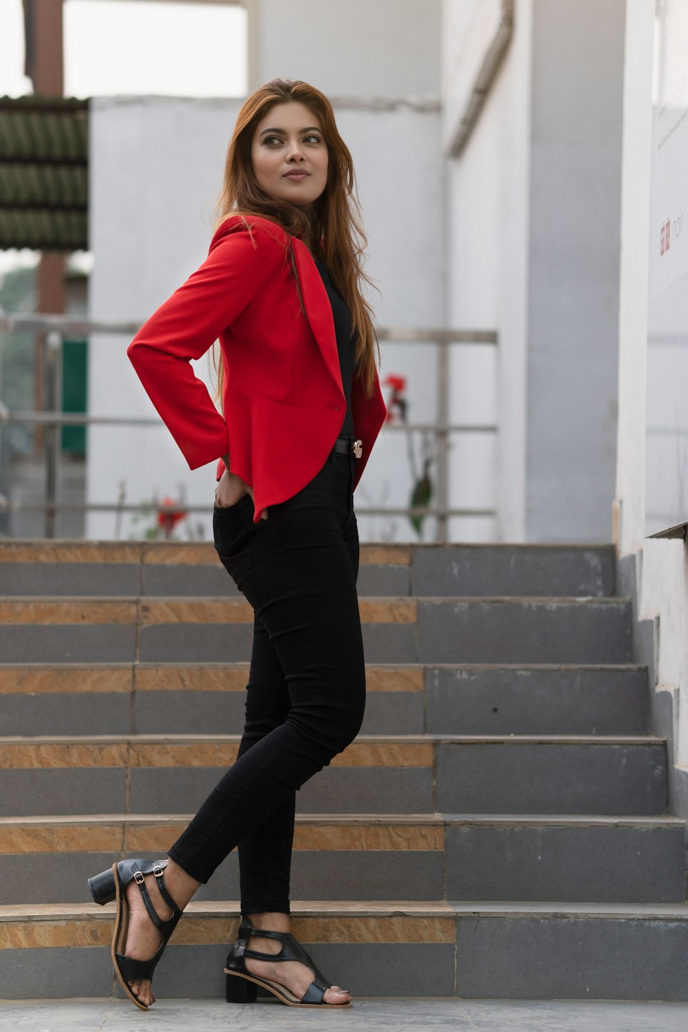 Woman in red blazer and black pants standing on gray concrete