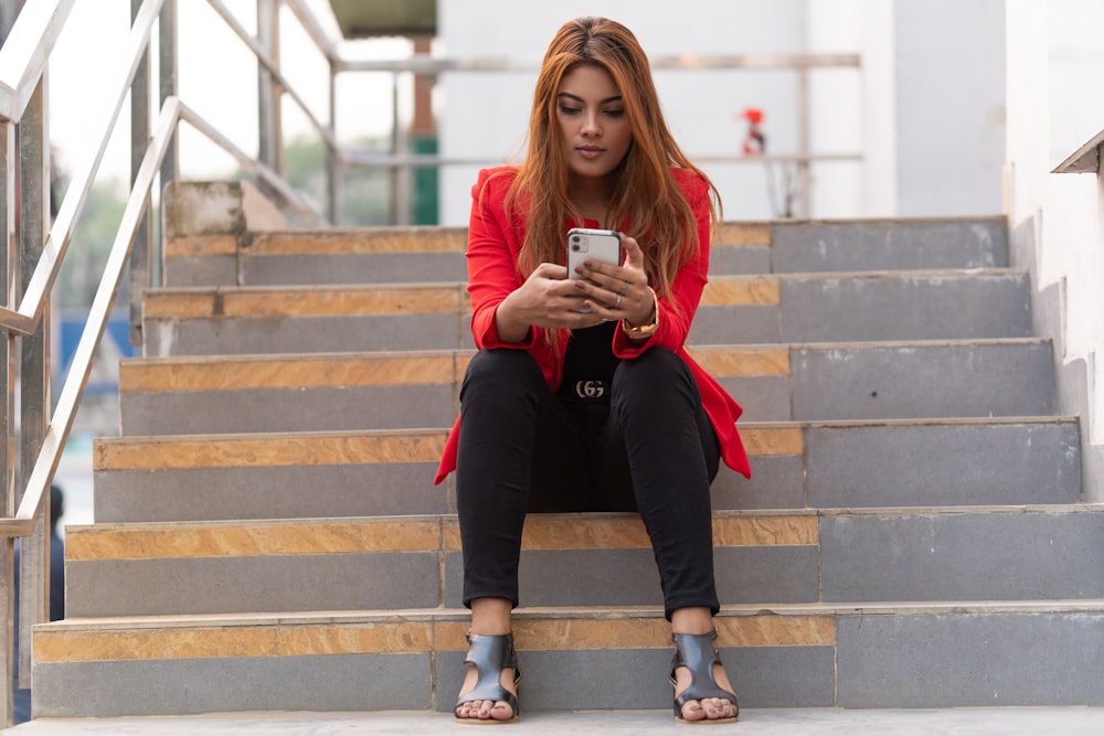 Mujer con camisa naranja de manga larga y pantalones negros sentada en las escaleras