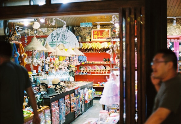 A bustling shop full of colorful collectibles and souvenirs, including traditional hats, masks, and decorative fans. The interior is adorned with various hanging items and a variety of toys arranged in racks. Warm lighting gives a cozy ambiance.