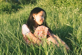 woman in yellow and red floral dress lying on green grass field during daytime