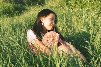 woman in yellow and red floral dress lying on green grass field during daytime