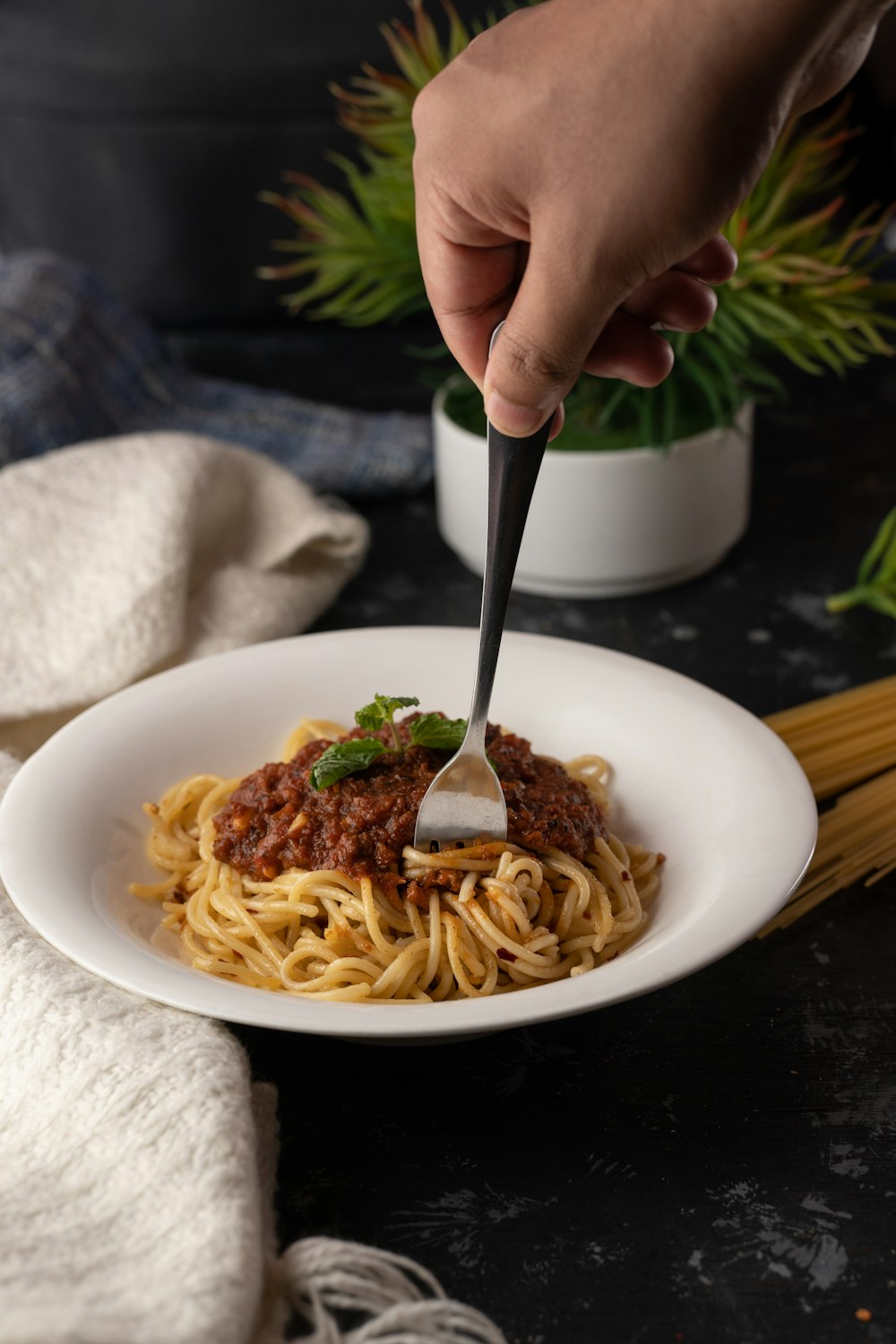 person holding silver fork and white ceramic plate with pasta