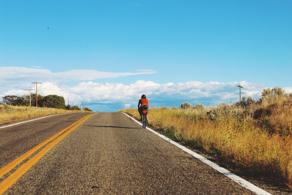 man in red shirt and black shorts walking on gray asphalt road during daytime