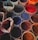 Several pots filled with vibrant powder pigments are arranged closely together, showcasing a variety of colors such as red, blue, purple, and orange. The pots appear to be made of clay or similar material, giving a rustic feel to the scene.