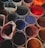 Several pots filled with vibrant powder pigments are arranged closely together, showcasing a variety of colors such as red, blue, purple, and orange. The pots appear to be made of clay or similar material, giving a rustic feel to the scene.