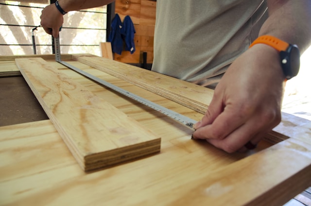 A skilled craftsman carefully measuring wood framing inside a bright, modern home under construction.