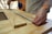 Close-up of a carpenter’s hands measuring a plywood sheet in a workshop.