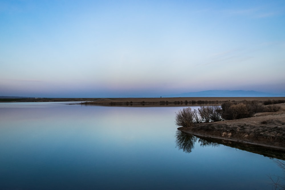 body of water near brown field under blue sky during daytime