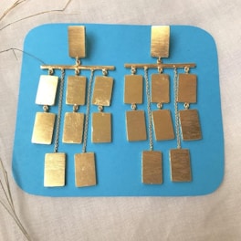 Close-up of a pair of handmade mid-century modern earrings resting on a wooden table with soft natural light.
