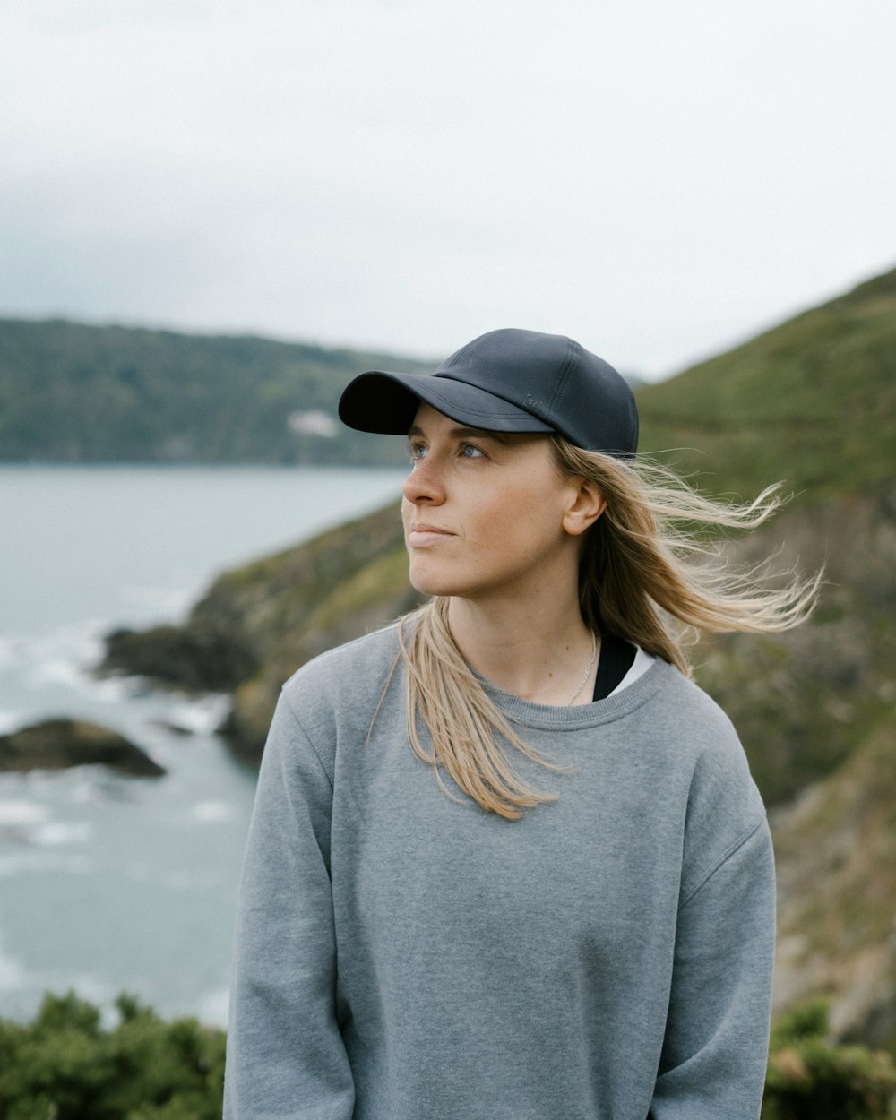 woman in gray sweater and black fedora hat standing near body of water during daytime