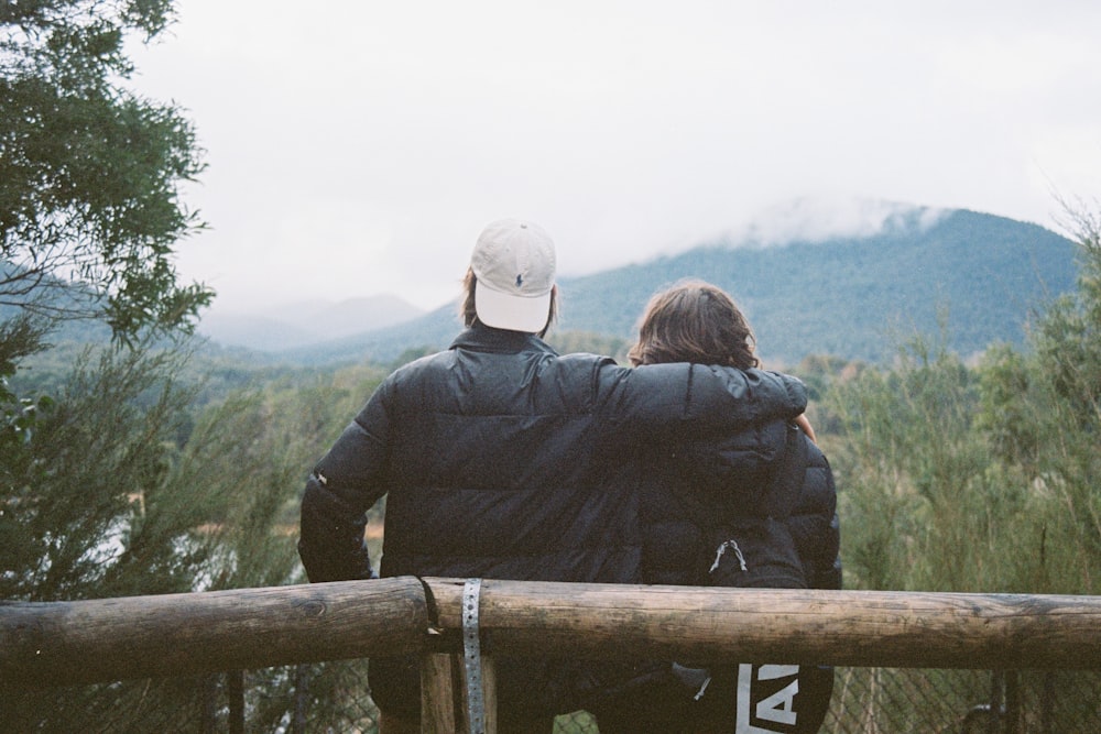 man and woman standing on brown wooden fence looking at green grass field during daytime