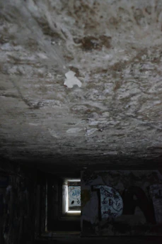 A dimly lit tunnel beneath the city, with faint graffiti and scattered belongings hinting at hidden lives.