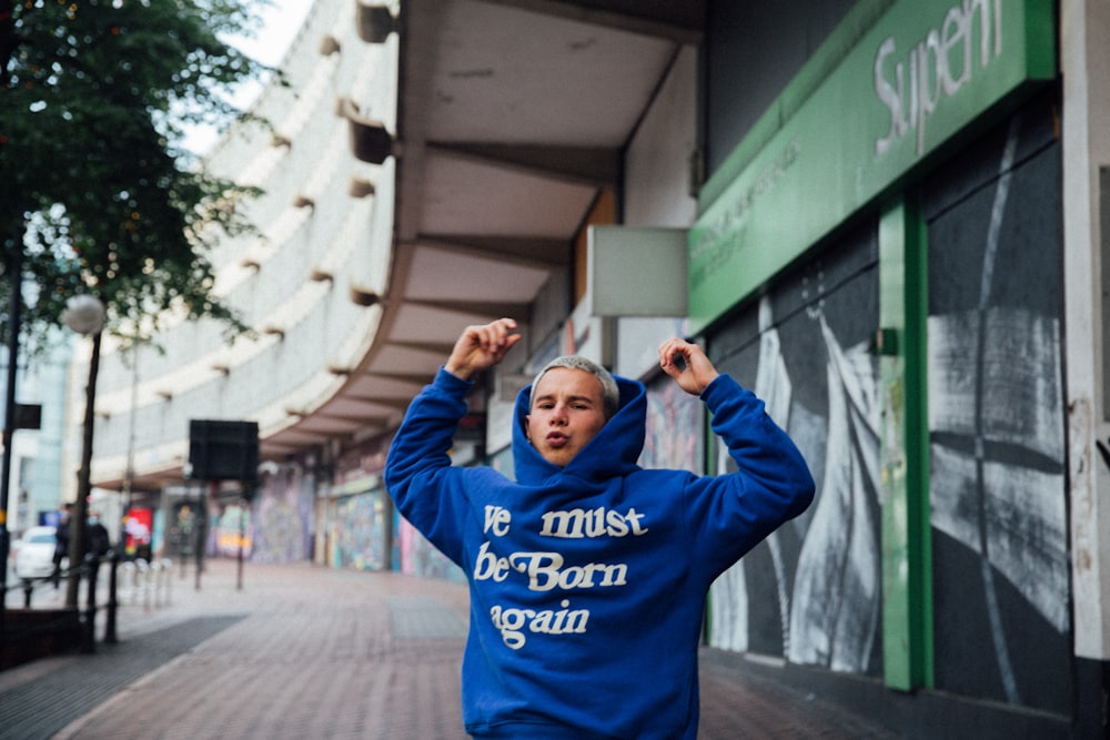 man in blue hoodie standing near green and white building during daytime