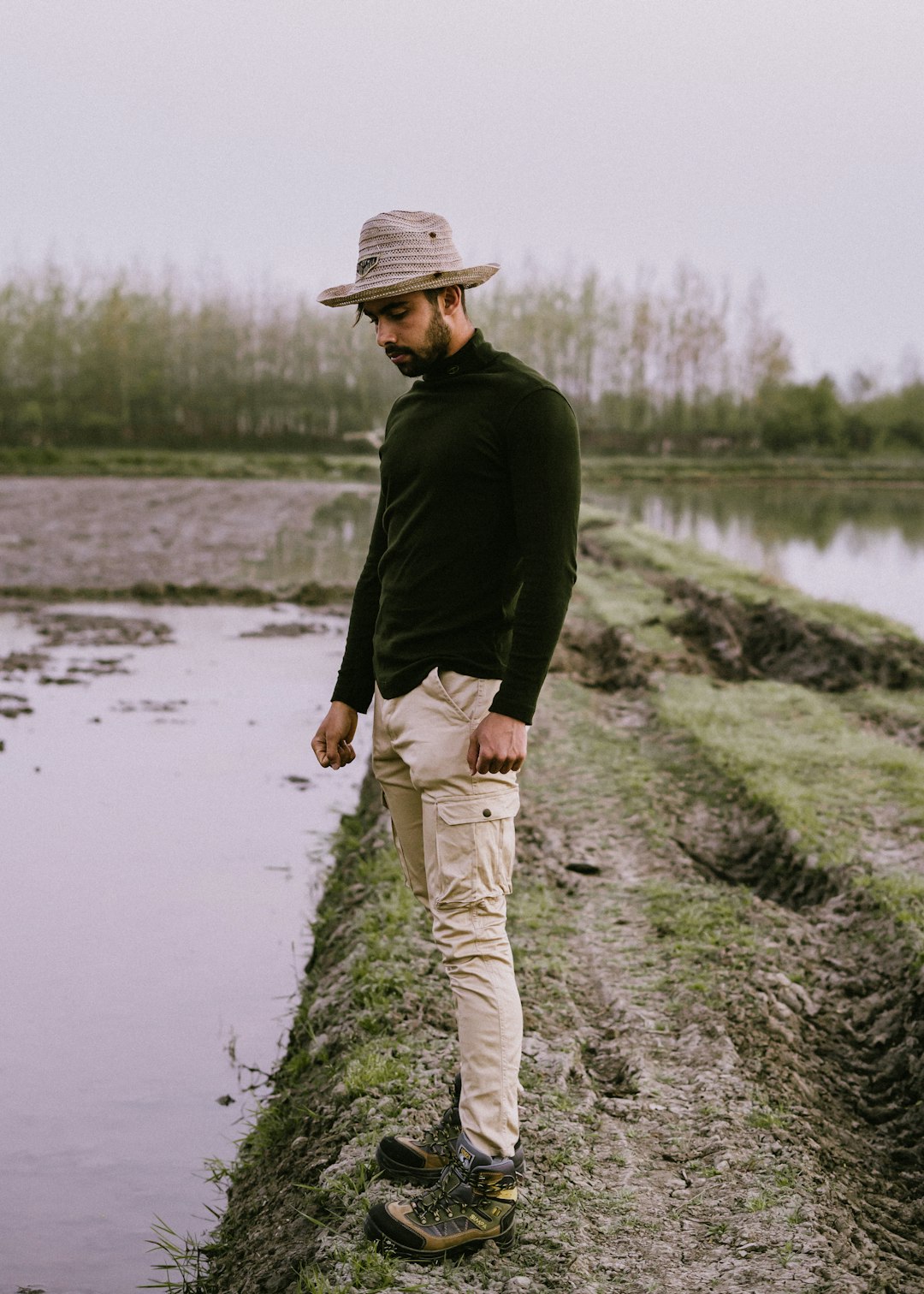 man in black jacket and white pants standing on gray rock near body of water during