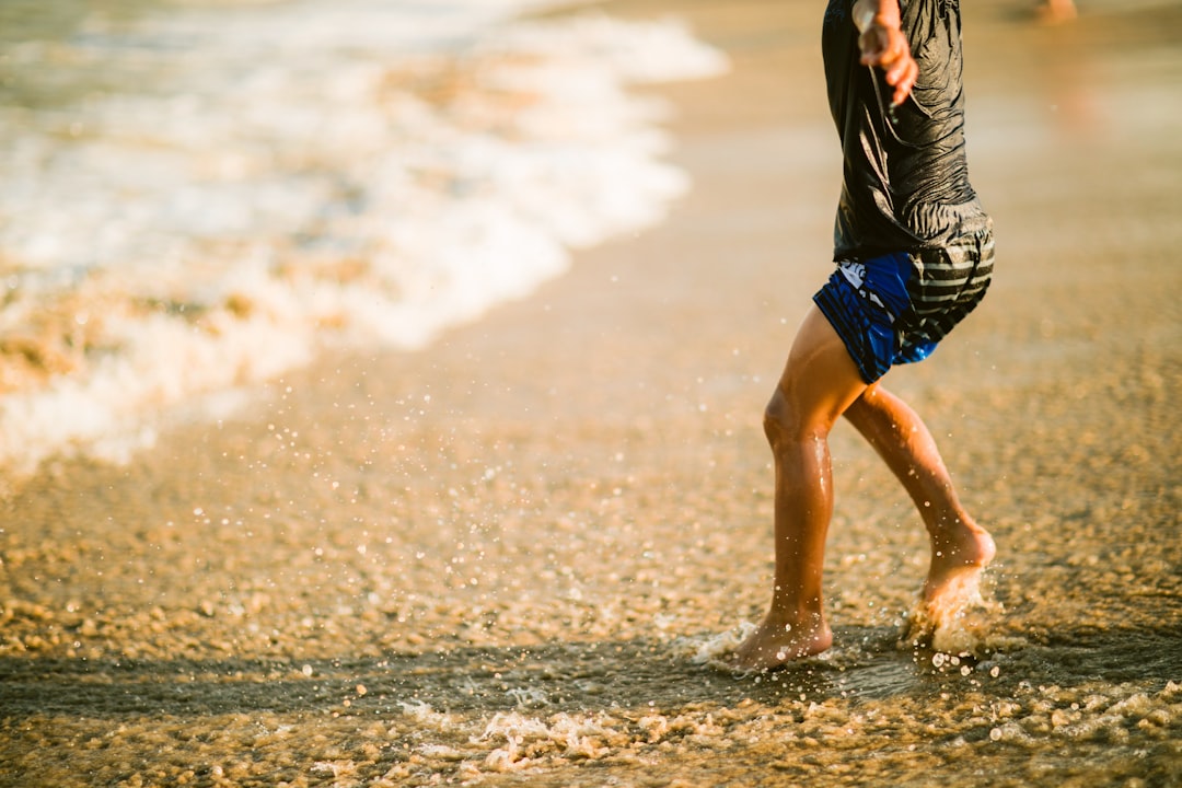 man in black and white stripe shirt and blue shorts running on beach during daytime