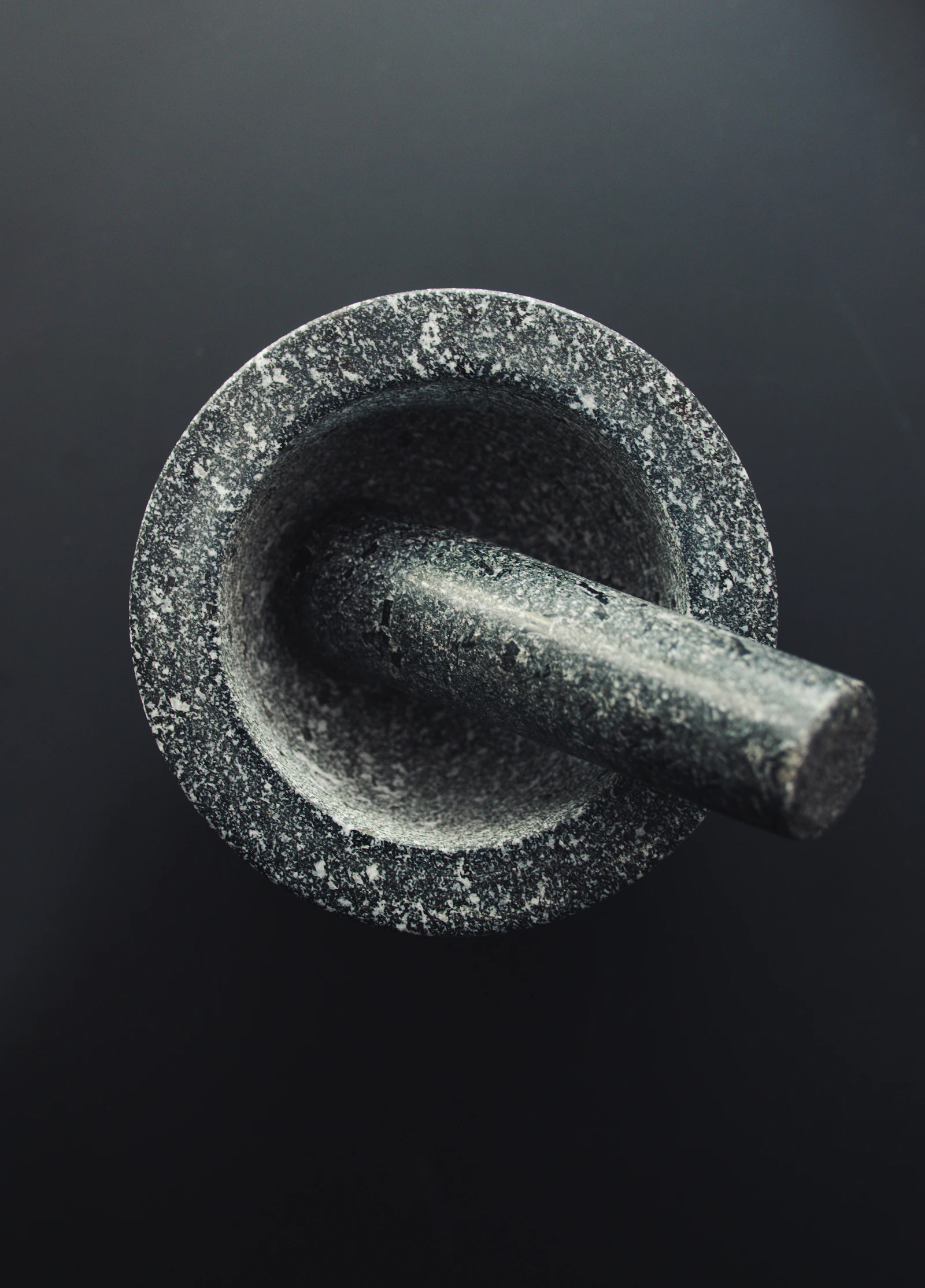 Top-down granite mortar and pestle on a deep slate ground