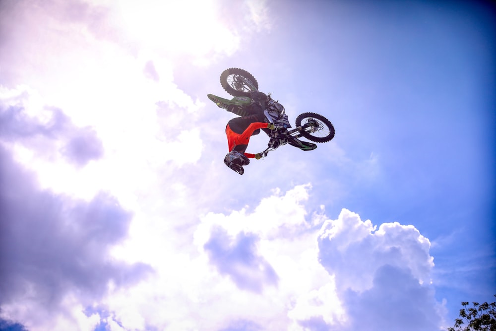 hombre montando en una bicicleta BMX negra haciendo acrobacias bajo el cielo nublado soleado azul y blanco durante